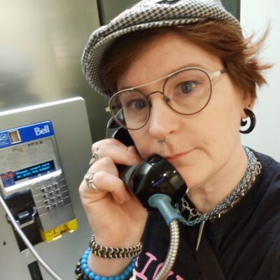 Image of Artist, Sara, with an old Bell telephone in a wall booth